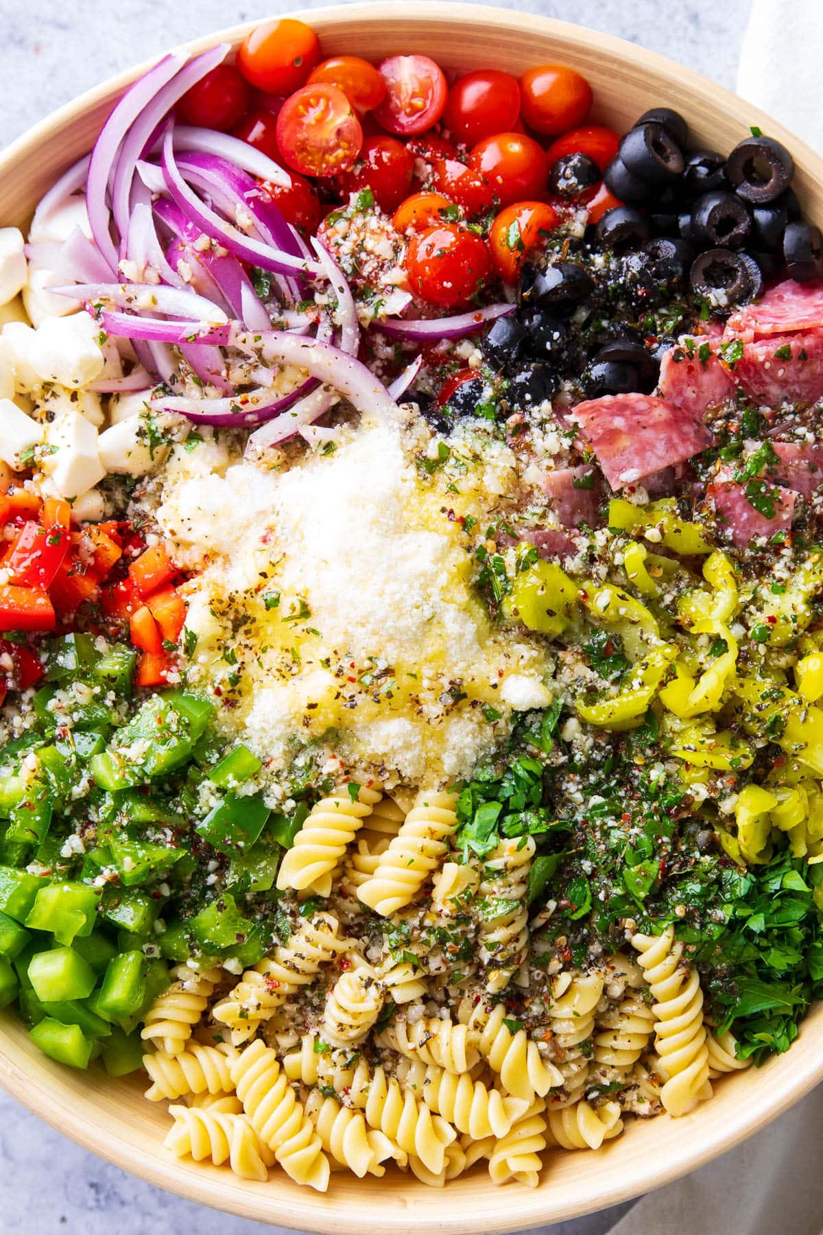 Close up of tomatoes, olives, pepperoncini, red onions, rotini, bell peppers, parsley, Parmesan, and mozzarella in a large serving bowl