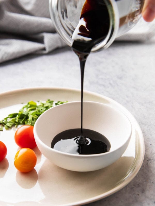 Pouring a jar of balsamic glaze into a serving bowl for dipping with veggies, bruschetta, and more.