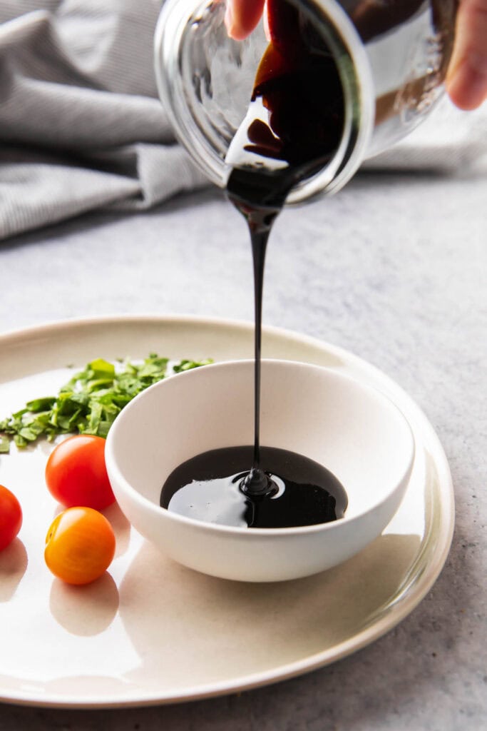 Pouring a jar of balsamic glaze into a serving bowl for dipping with veggies, bruschetta, and more.