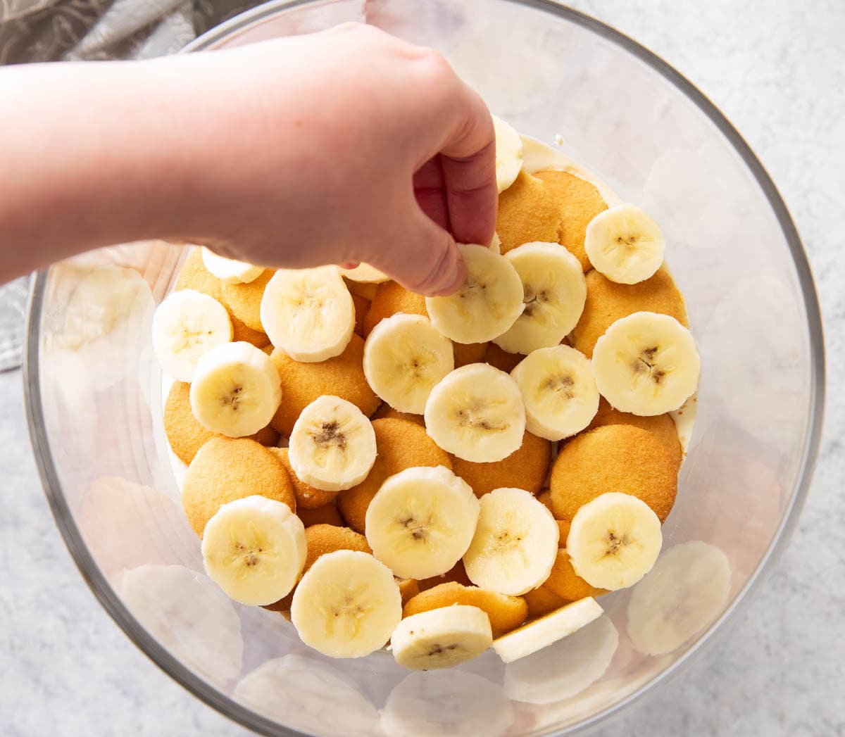 One photo showing How to Layer Banana Pudding - placing sliced bananas over the vanilla wafers and pudding