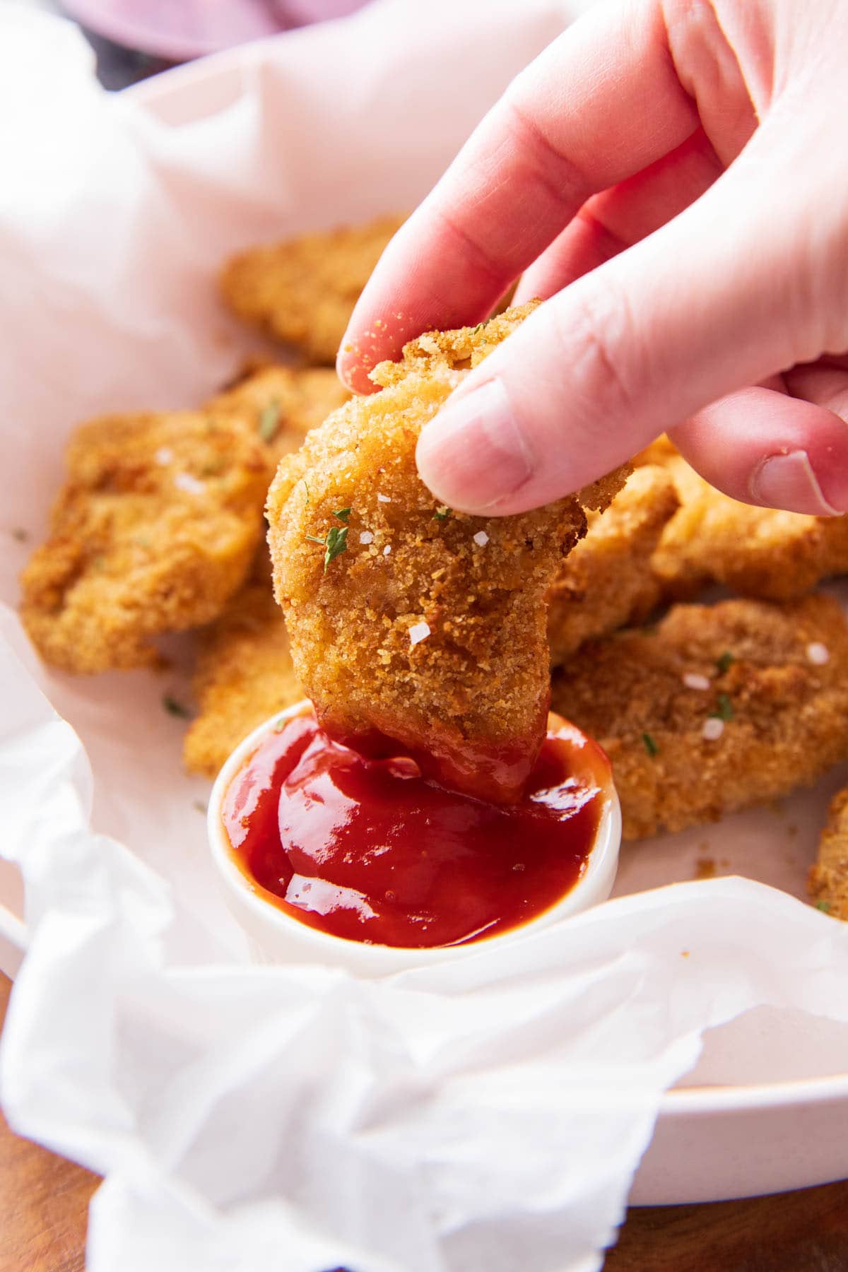 Hand dipping air fryer chicken nuggets into a bowl of ketchup