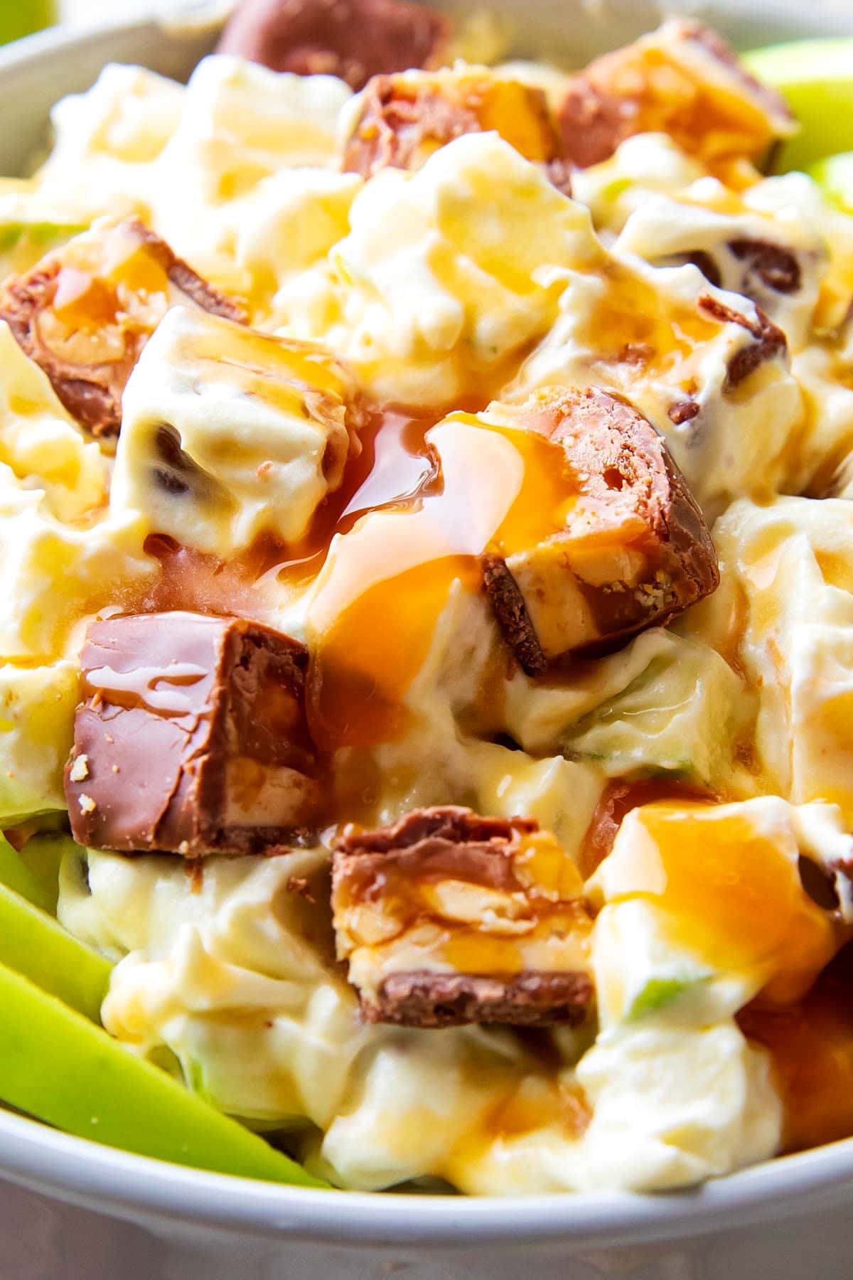 Close up of caramel apple snickers salad to show drizzle of caramel on top of creamy cool whip salad dressing over tart apples.