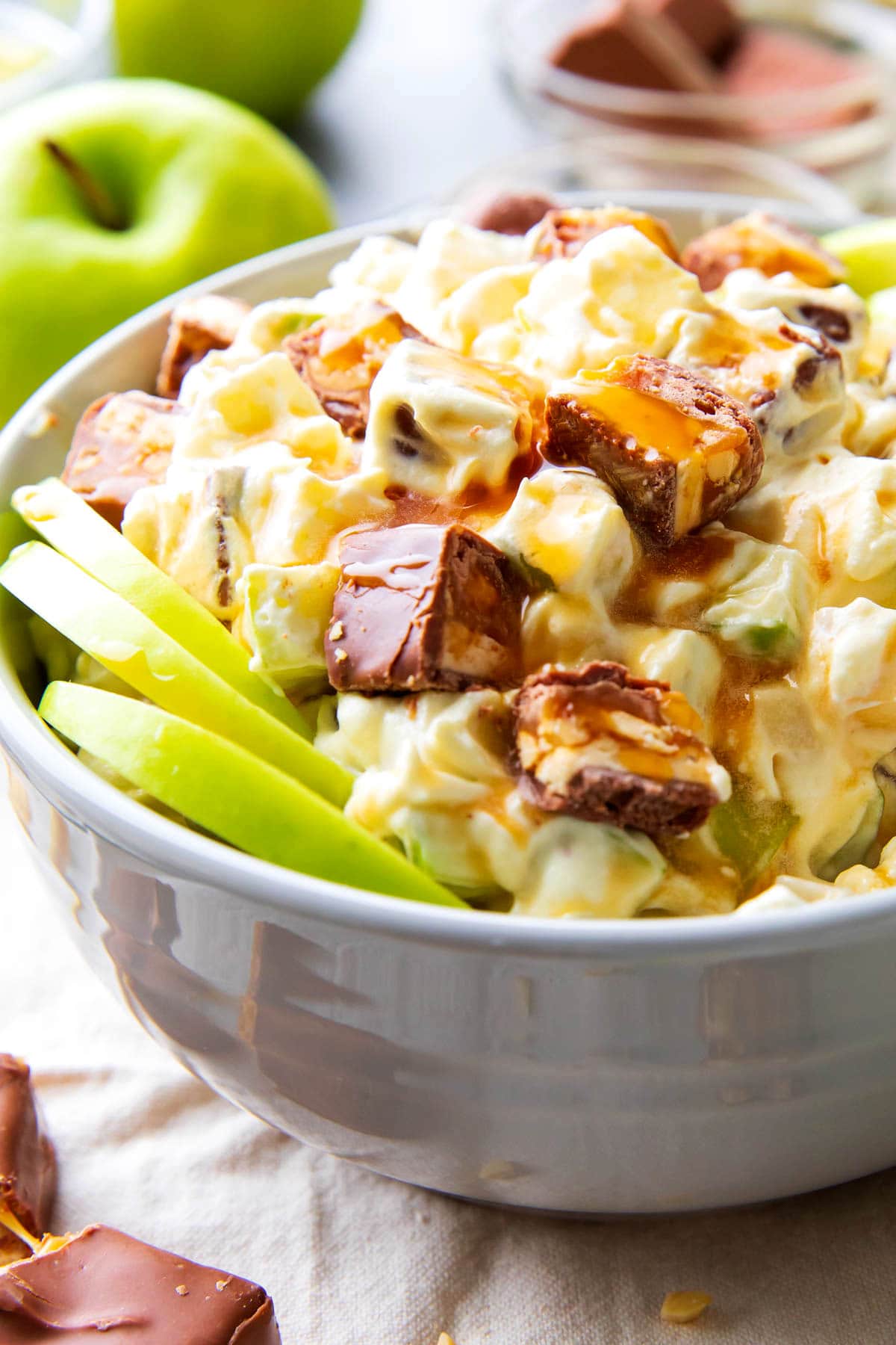Snickers apple salad with Cool whip served in a dessert salad bowl with apples and caramel.