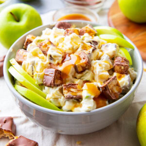 featured image with Snickers Salad served with caramel sauce, apple slices, and Snickers.