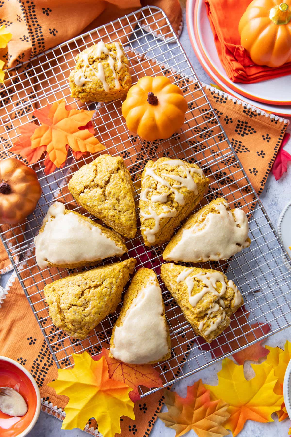 a fall treats table covered in pumpkin scones with glaze and some with sugar topping