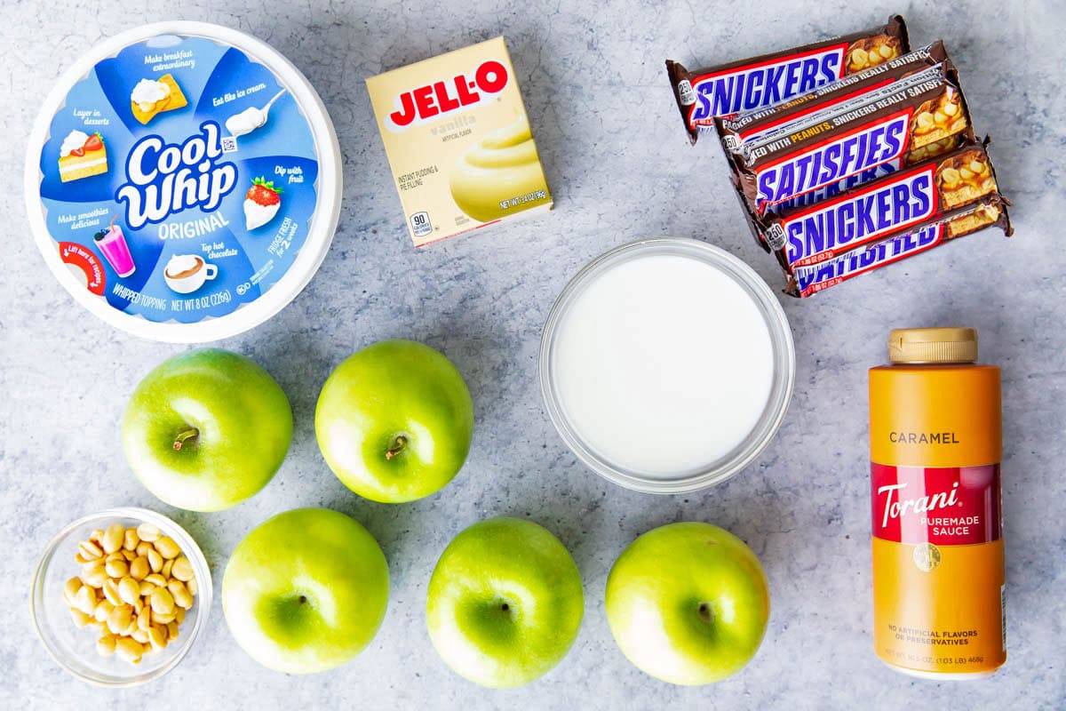 Snickers Salad with vanilla pudding, apples, candy bars, peanuts, caramel topping, milk, and other ingredients.