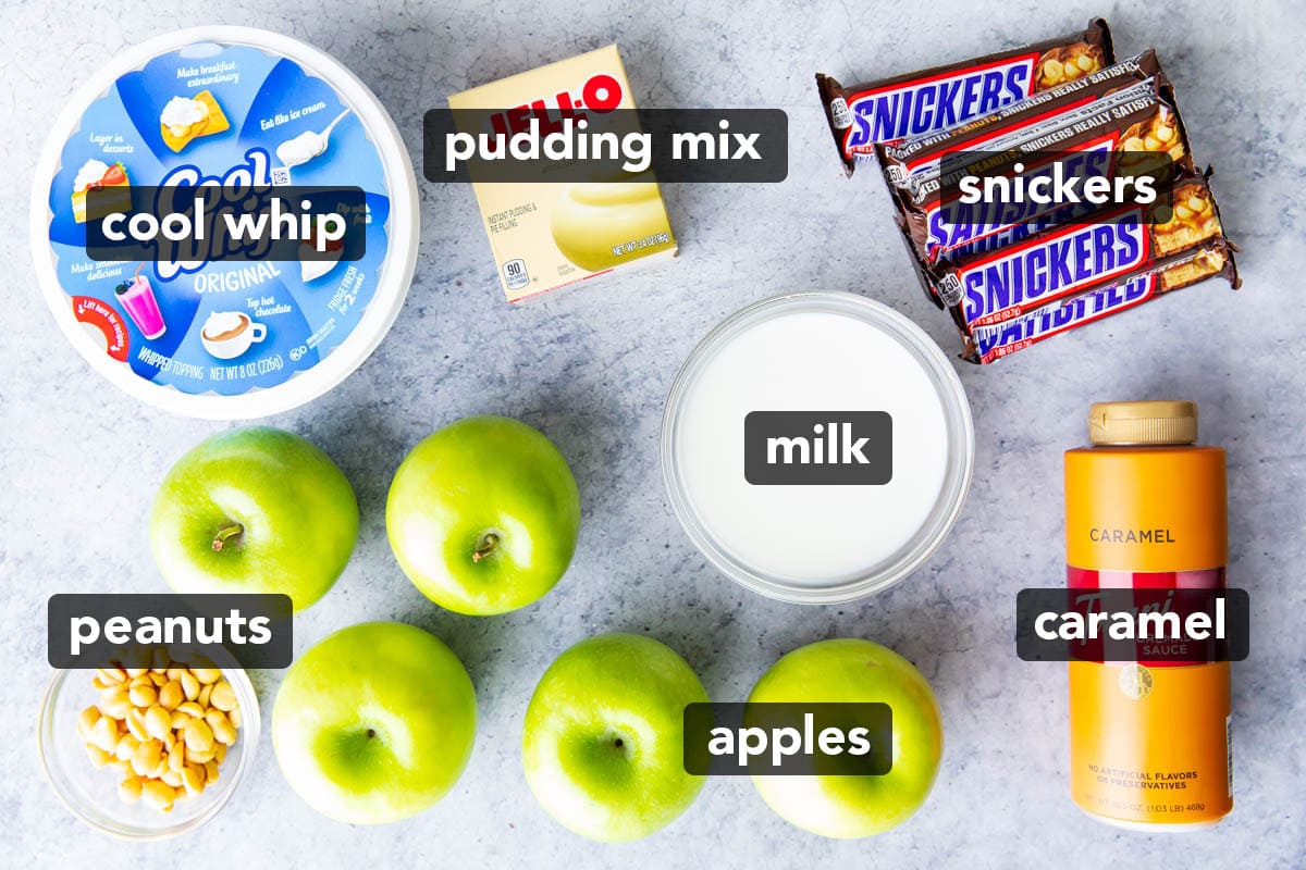 Snickers Salad Recipe ingredients including Granny Smith apples, Cool Whip, instant pudding mix, snickers candy bars, caramel sauce, milk, and peanuts