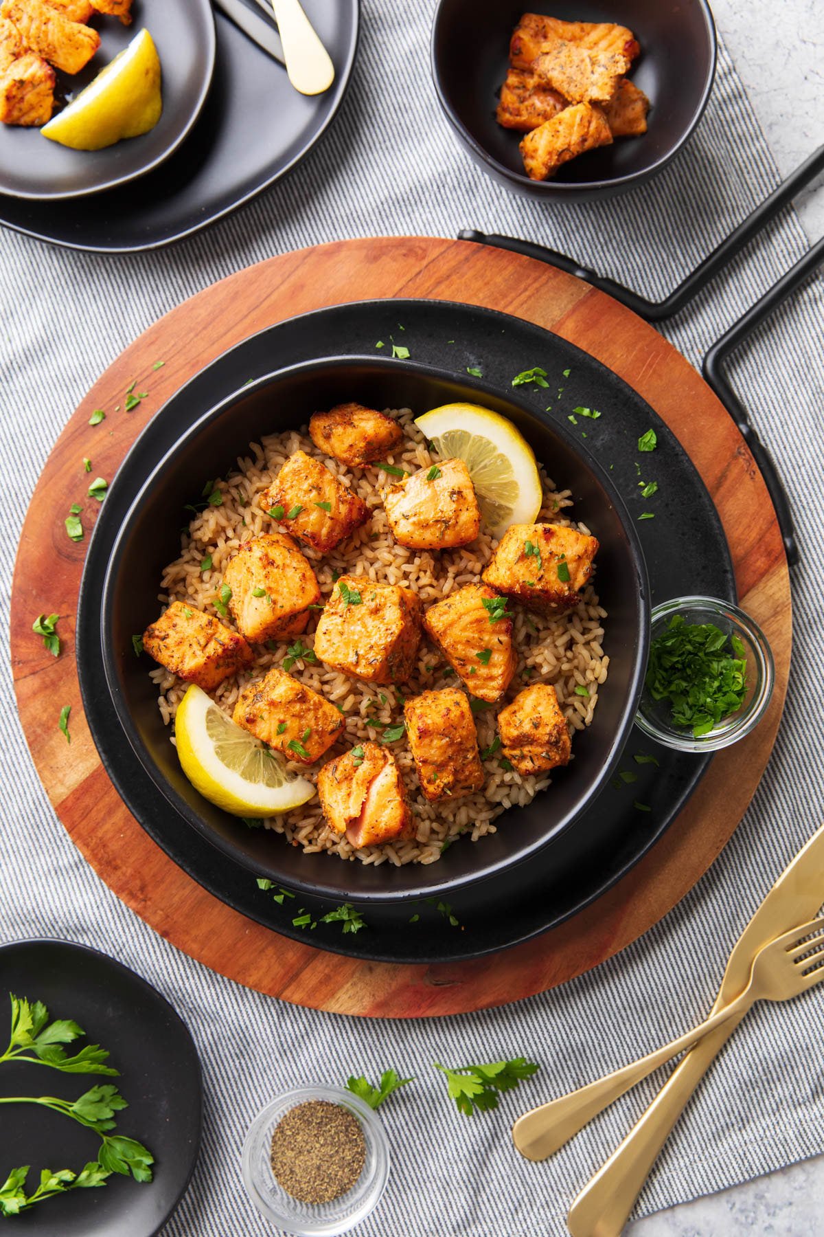 Air Fryer salmon bites served over a bed of brown rice with lemon wedges and garnish on a dinner table with forks and knives.