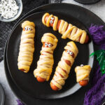 spooky halloween table set with this hot dog mummies recipe, purple and black gauze, and a spiderweb dipping sauce