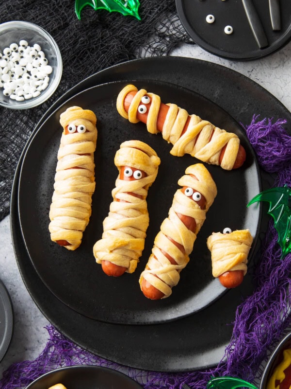 spooky halloween table set with this hot dog mummies recipe, purple and black gauze, and a spiderweb dipping sauce