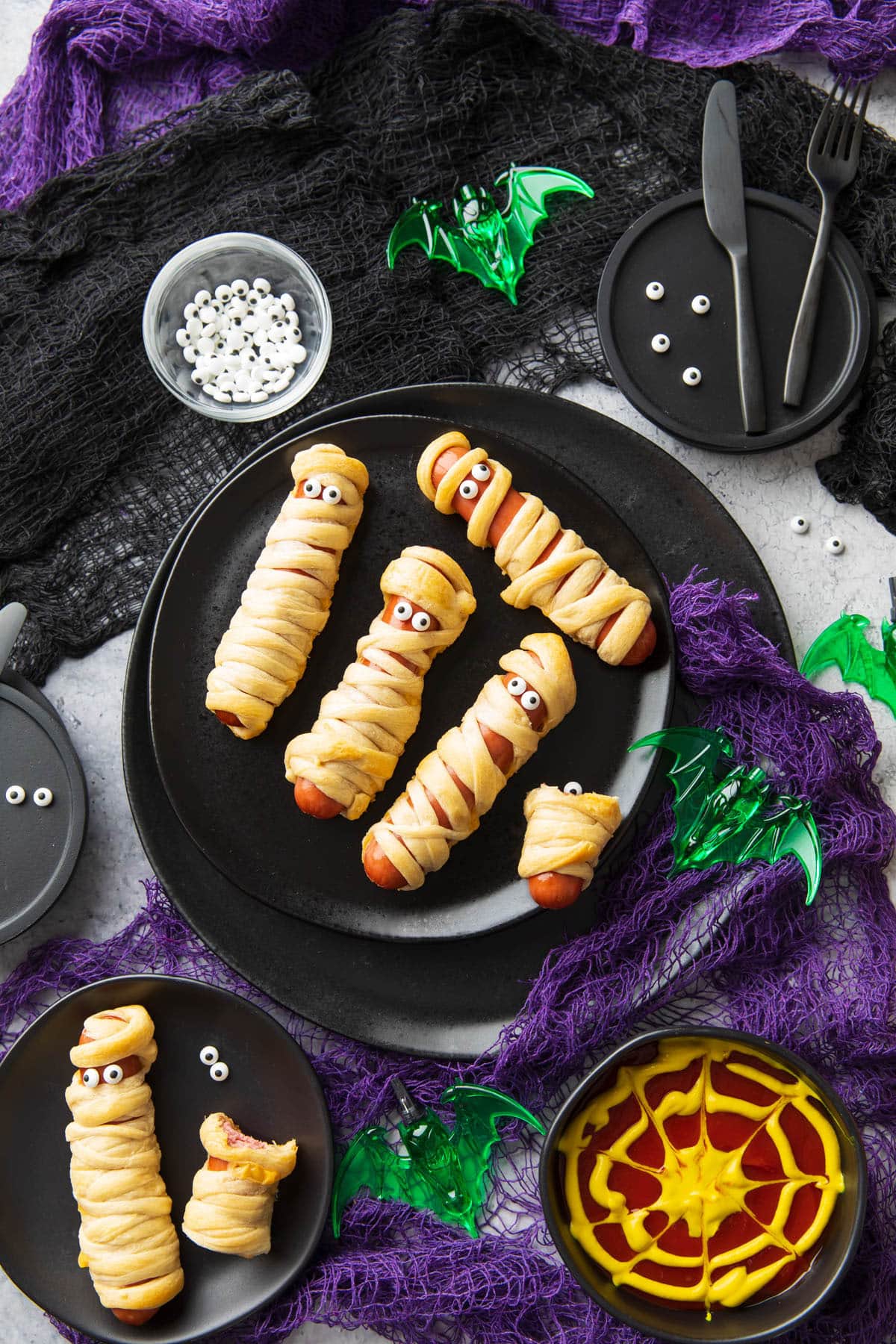 spooky halloween table set with this hot dog mummies recipe, purple and black gauze, and a spiderweb dipping sauce