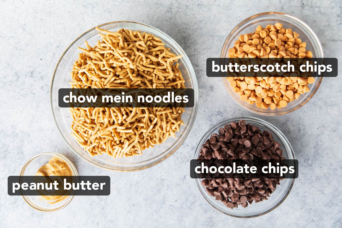 Haystack cookie recipe ingredients scooped into bowls including chow mien noodles, chocolate chips, butterscotch chips, and peanut butter.