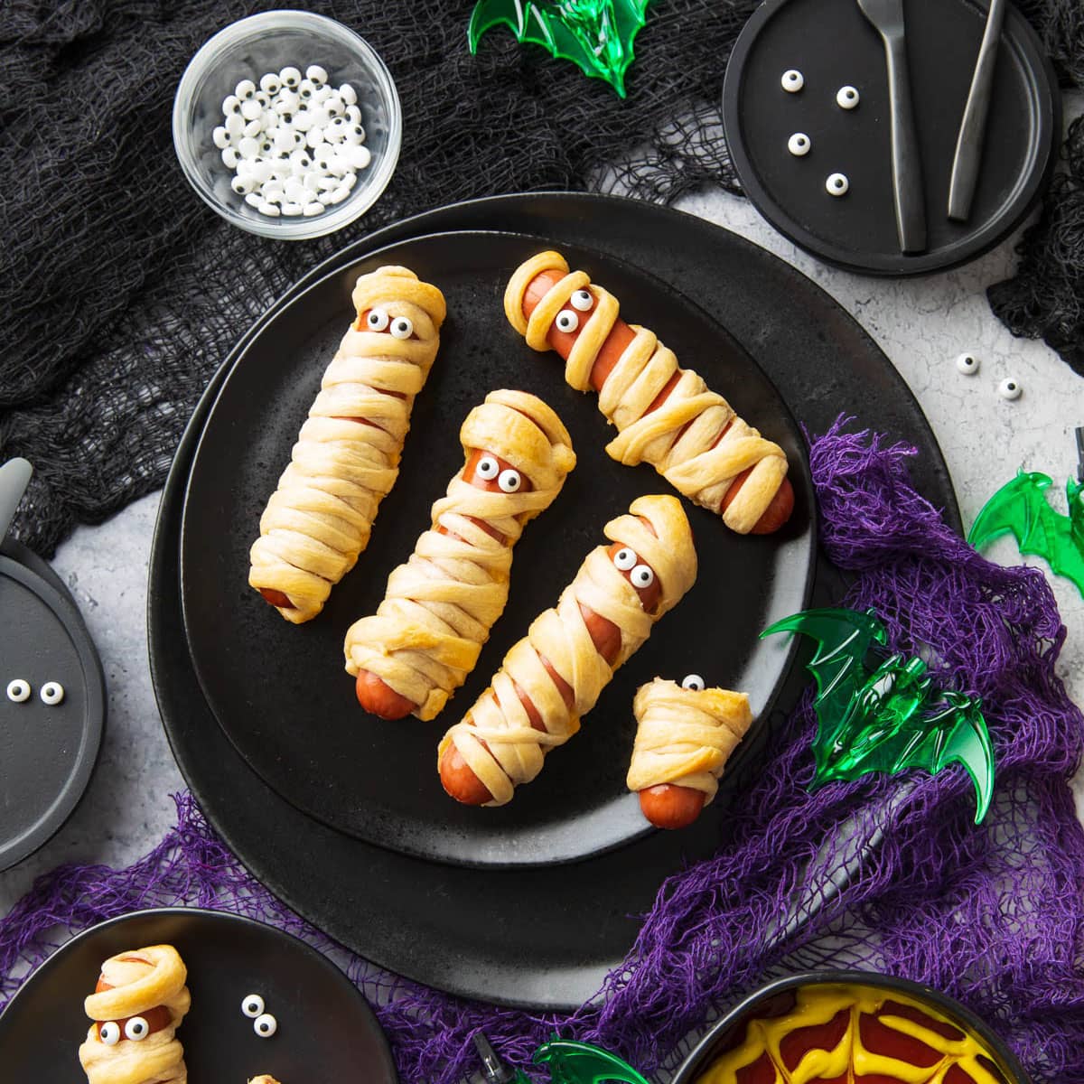 spooky halloween table set with this hot dog mummies recipe, purple and black gauze, and a spiderweb dipping sauce