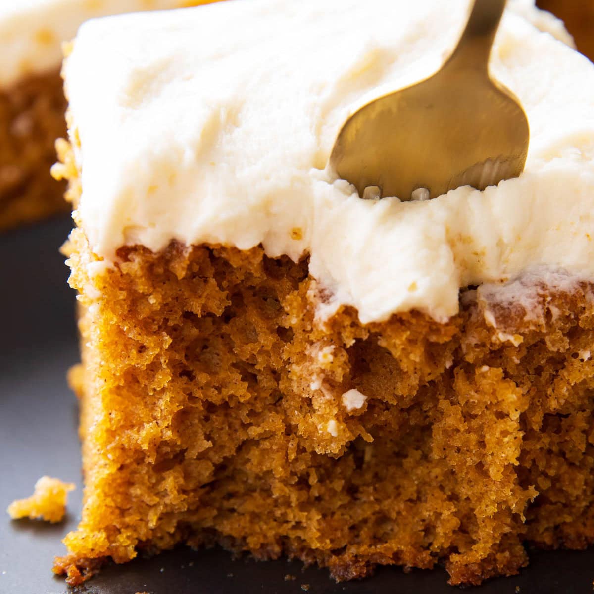 close up of a fork cutting into moist pumpkin cake with cream cheese frosting