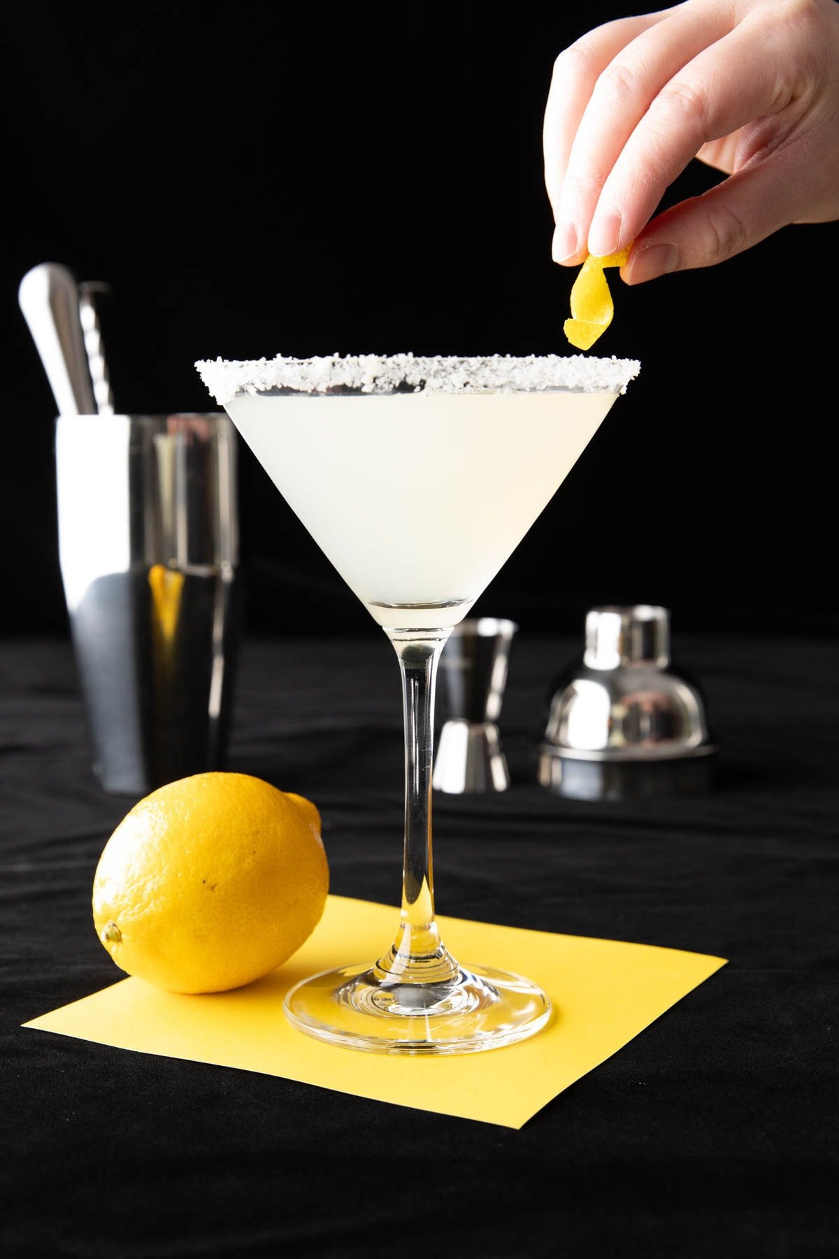 Hand placing a lemon twist onto the lemon sugared rim of a Lemon Drop.