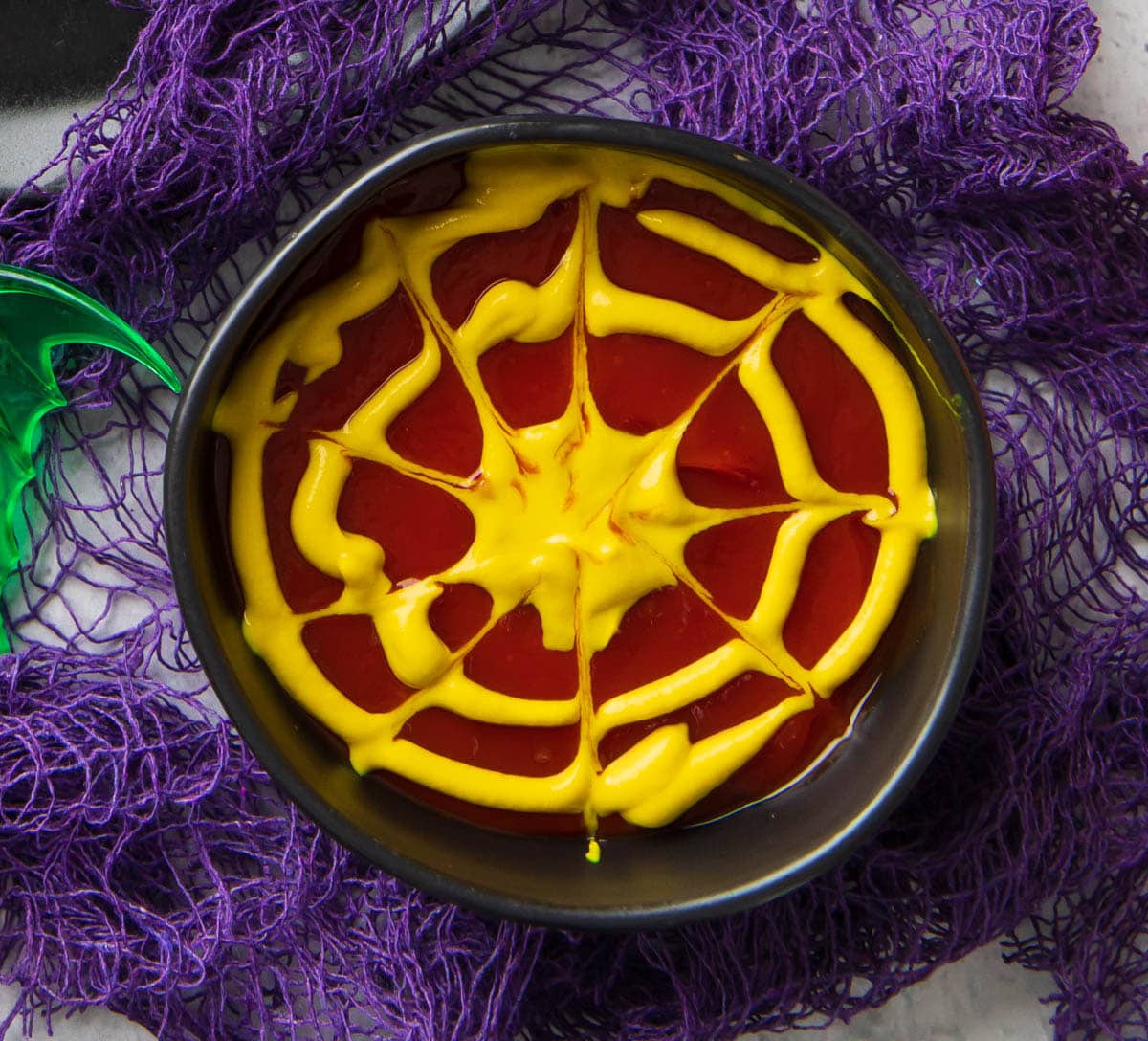 Spiderweb Dipping Sauce - a bowl of spiderweb dipping sauce shows how to draw mustard over ketchup as a festive condiment for this halloween finger food