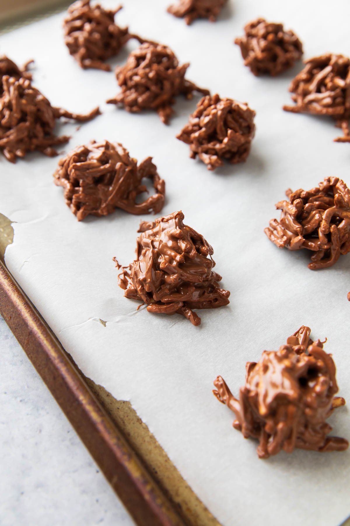 Lines of haystack cookies - Neatly scooped no bake Christmas cookies on a parchment lined baking sheet.