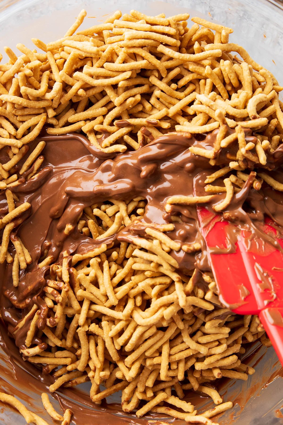 Folding melted chocolate and butterscotch mixture with chow mien noodles in mixing bowl.