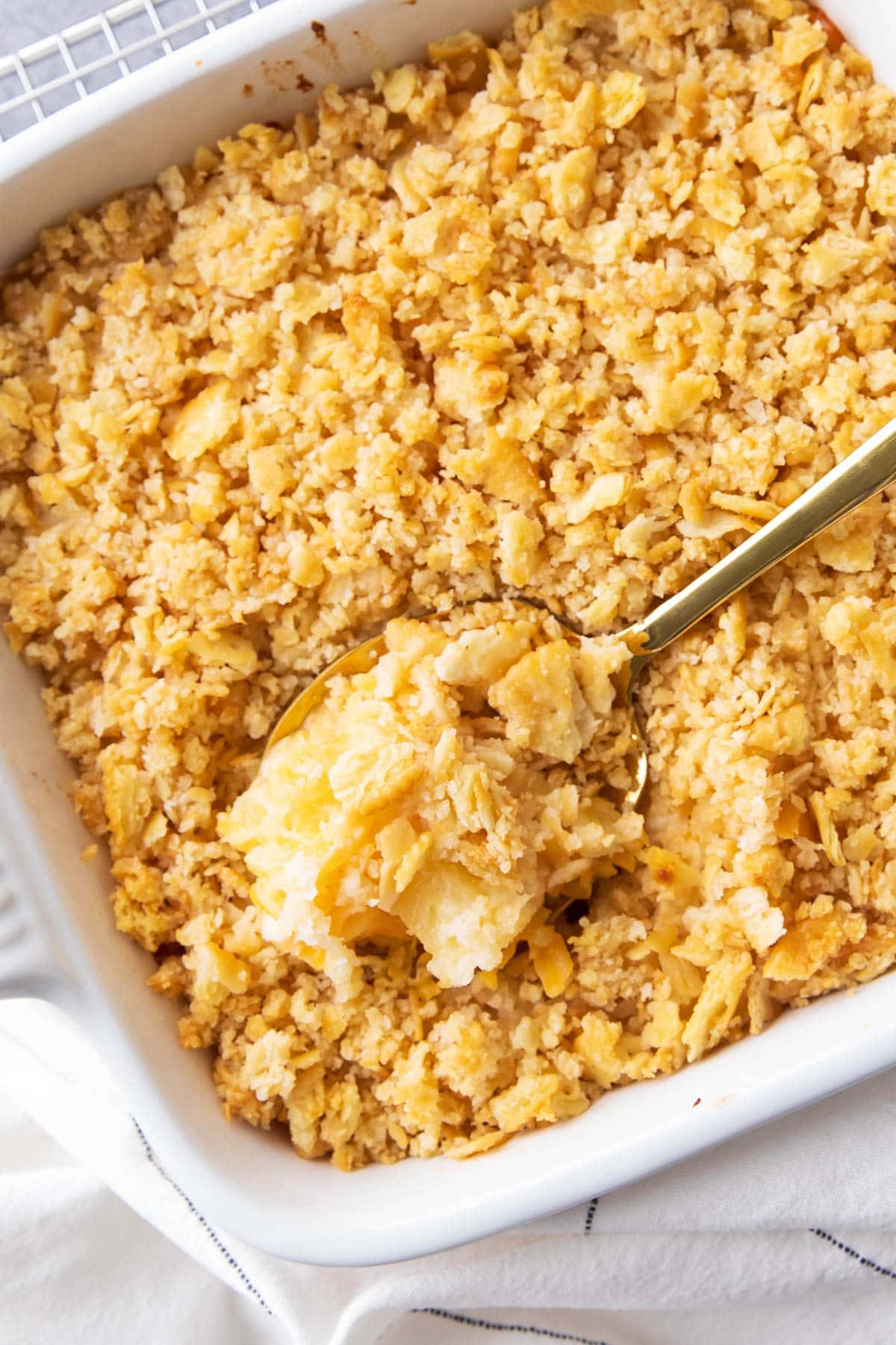 Spooning a serving of Pineapple Casserole fresh-baked in a white casserole dish