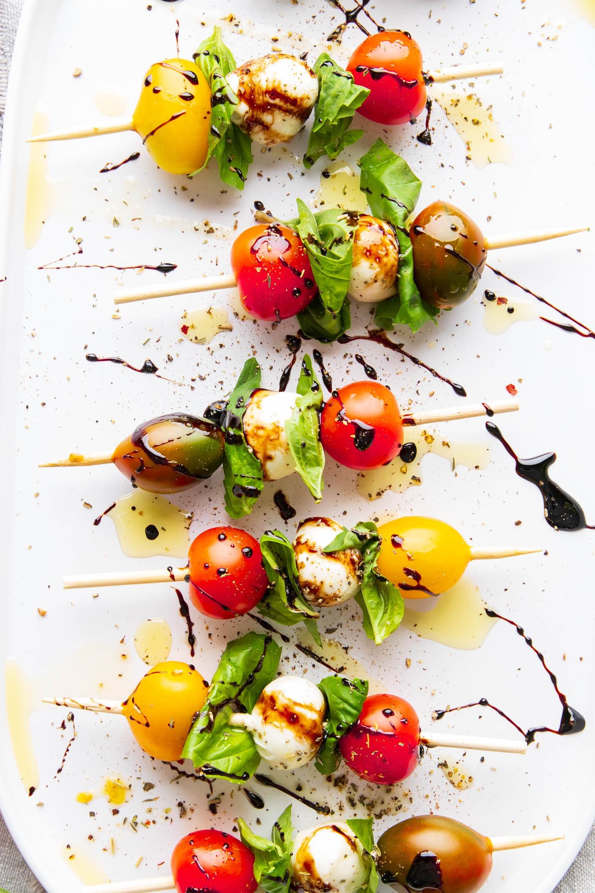 Balsamic glaze, olive oil, and Italian seasoning garnishes this easy fancy appetizer on mini skewers.