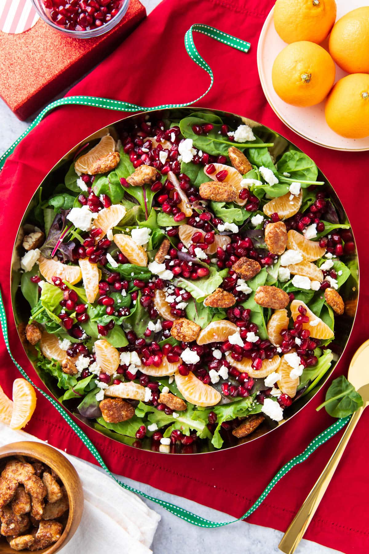 Serving bowl packed with spinach, lettuce, arugula, fruits, pecans, and feta cheese topped with dressing.