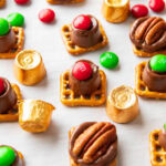 Angled photo of Rolo pretzels dotted with M&M candies and pecan halves served with gold foil-wrapped Rolos.