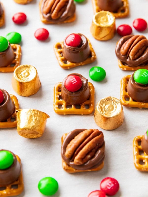 Angled photo of Rolo pretzels dotted with M&M candies and pecan halves served with gold foil-wrapped Rolos.