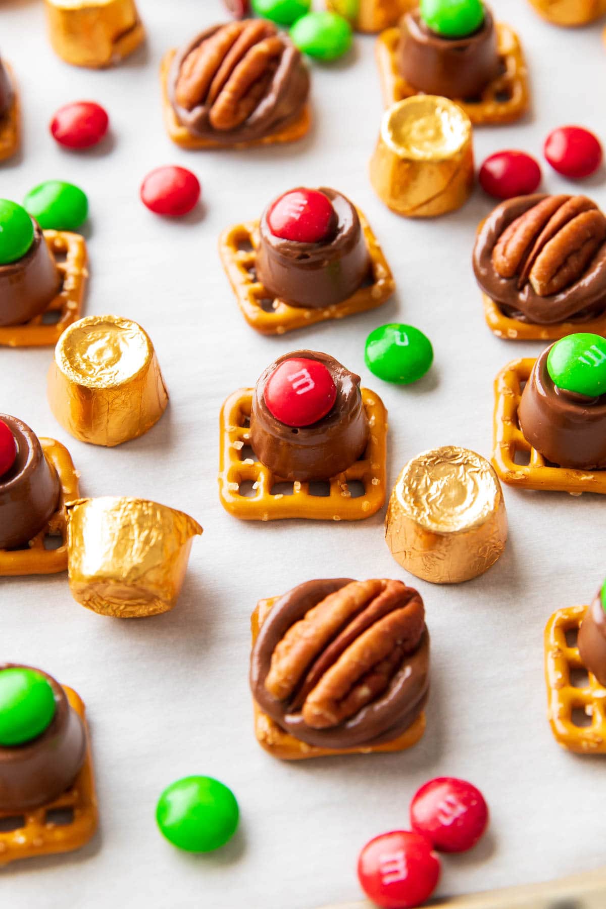 Angled photo of Rolo pretzels dotted with M&M candies and pecan halves served with gold foil-wrapped Rolos.