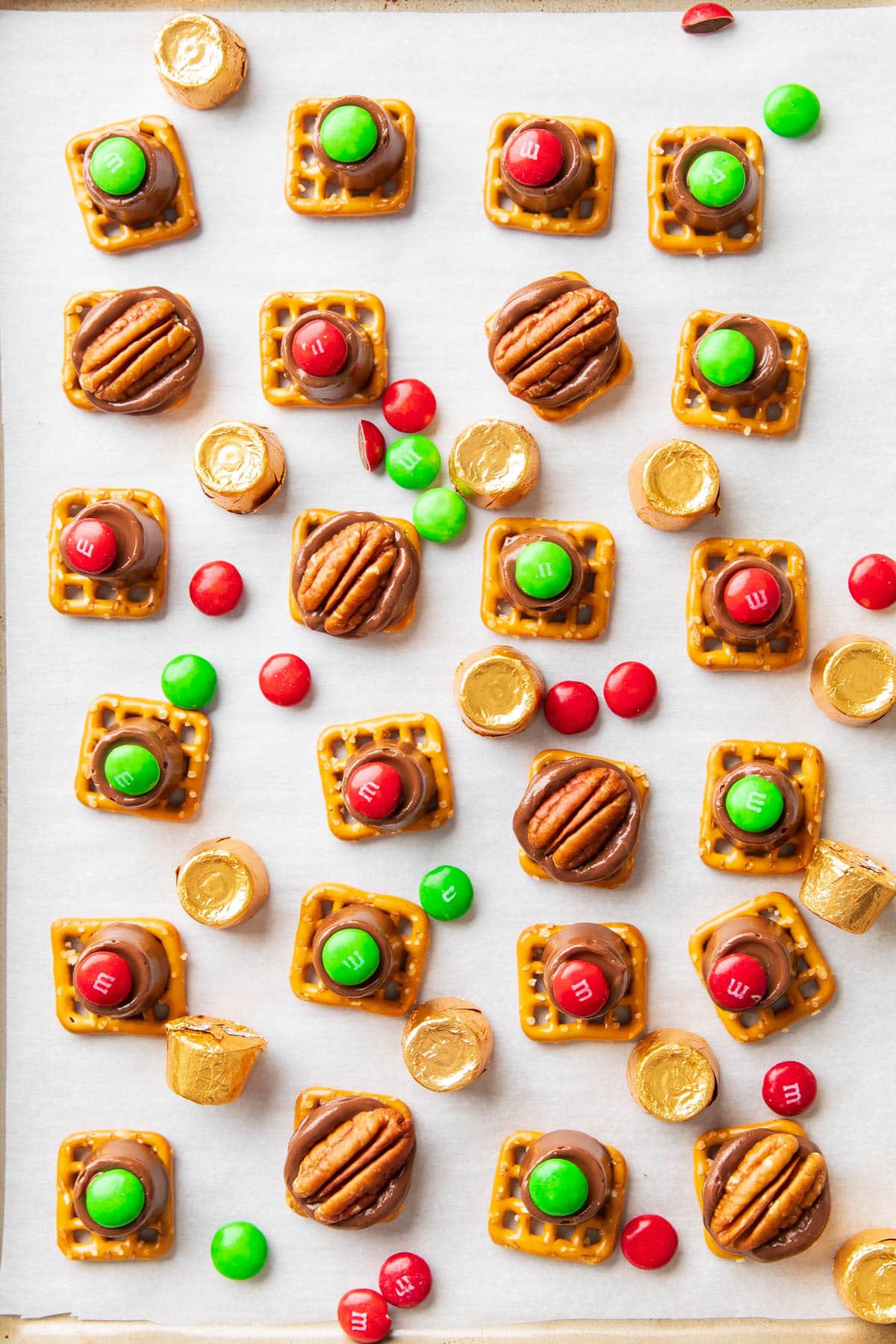 A lined baking sheet with red and fold M&M’s pressed into melted Rolo candies on top of pretzels for this Rolo Pretzel recipe.