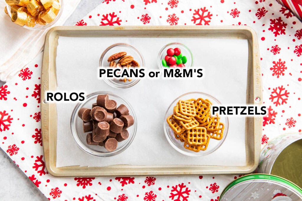 The ingredients for this pretzel Rolo recipe in glass bowls, including pretzels, unwrapped Rolo candies, M&M’s and pecans.