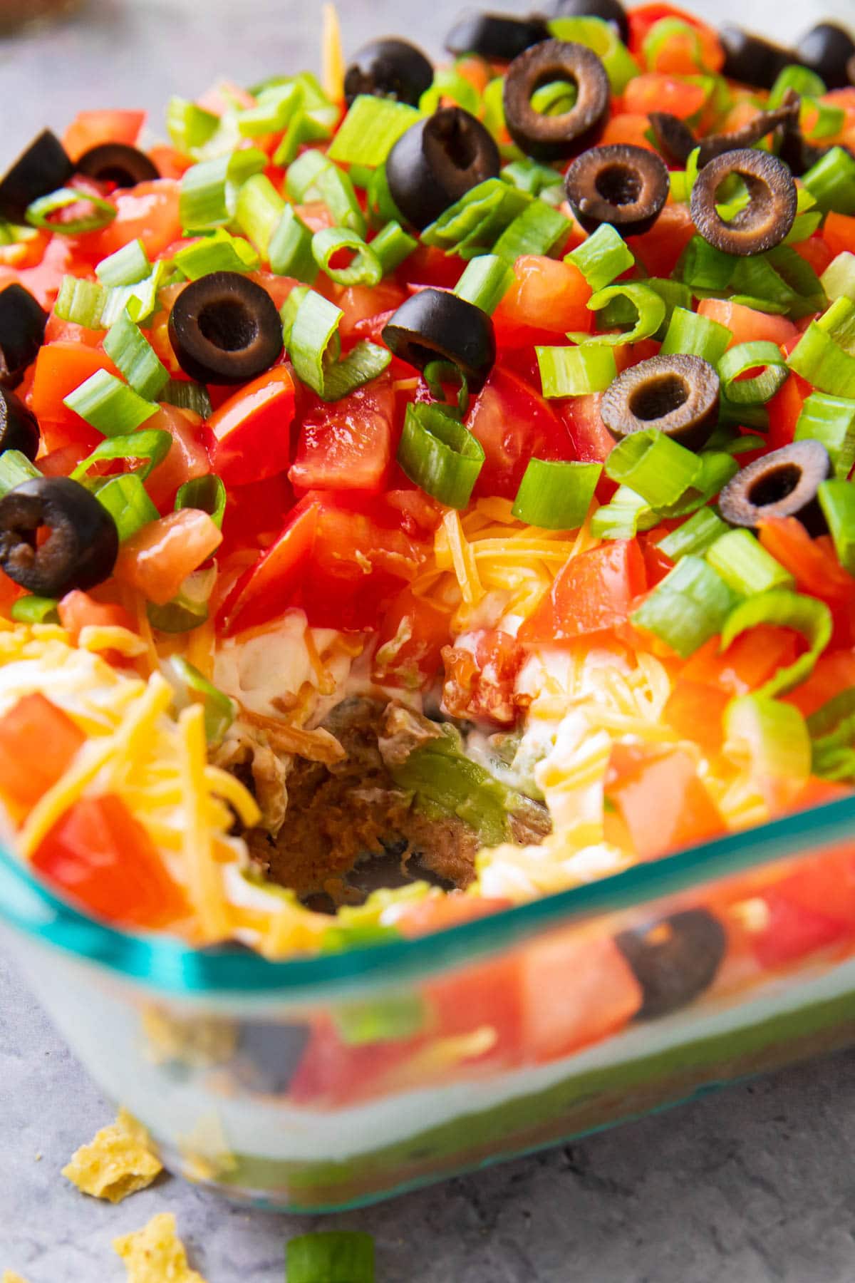 Semi-eaten 7 Layer Dip recipe with tomatoes, sour cream, refried beans, green onions, and cheese