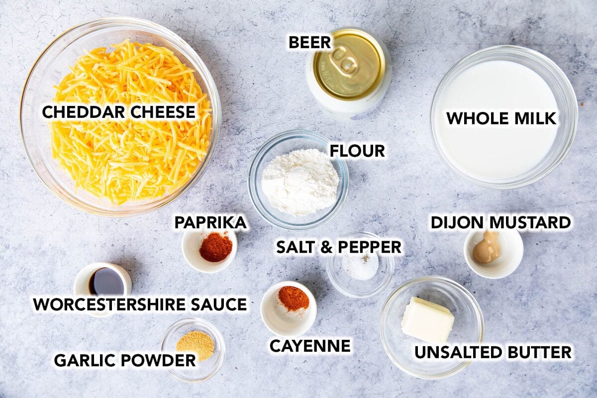 Pretzel beer cheese dip ingredients in prep bowls including shredded cheese, flour, beer, Worcestershire sauce, mustard, paprika, and more spices.