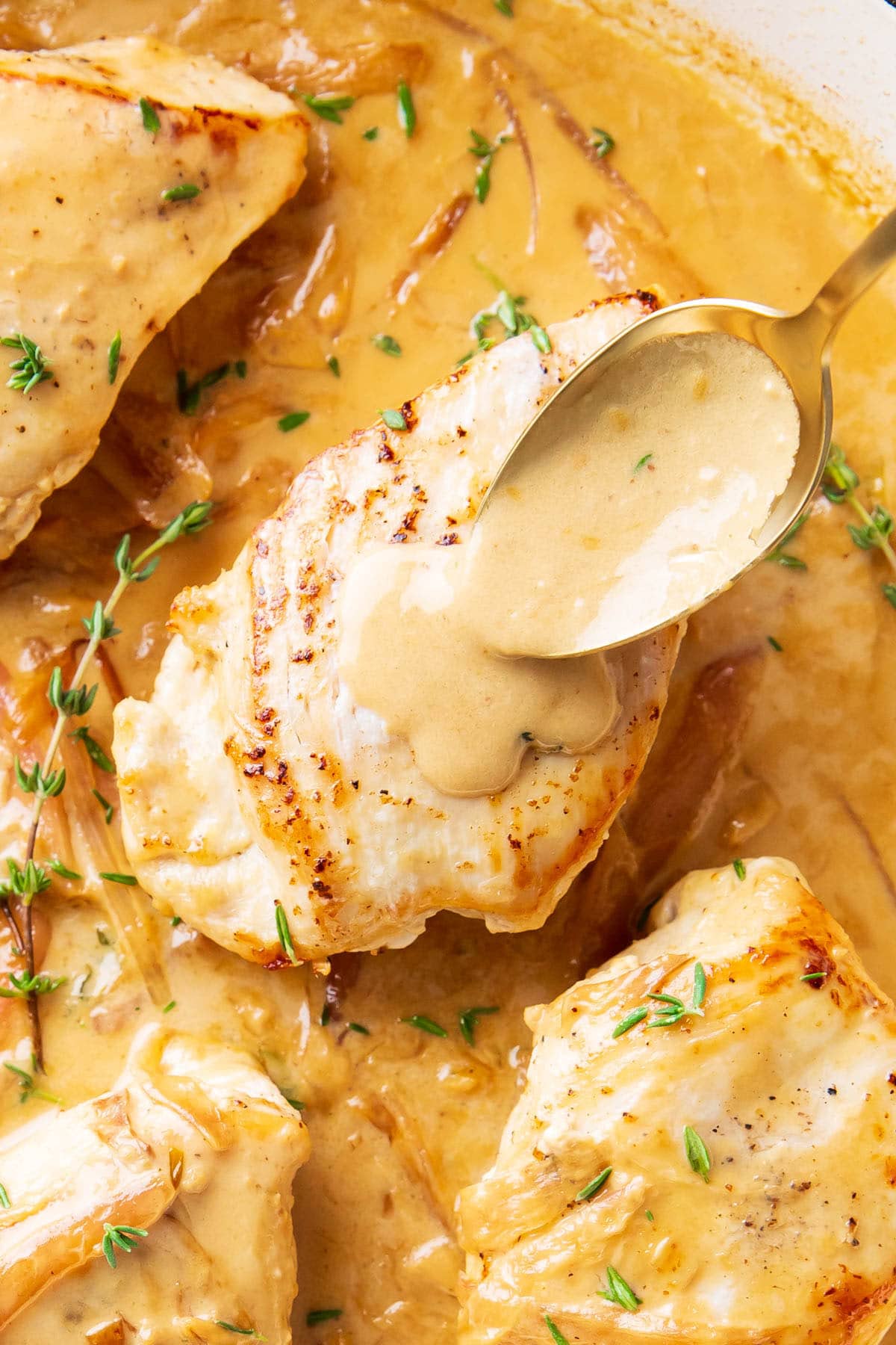 Someone spooning Dijon Chicken sauce over this grilled chicken breasts