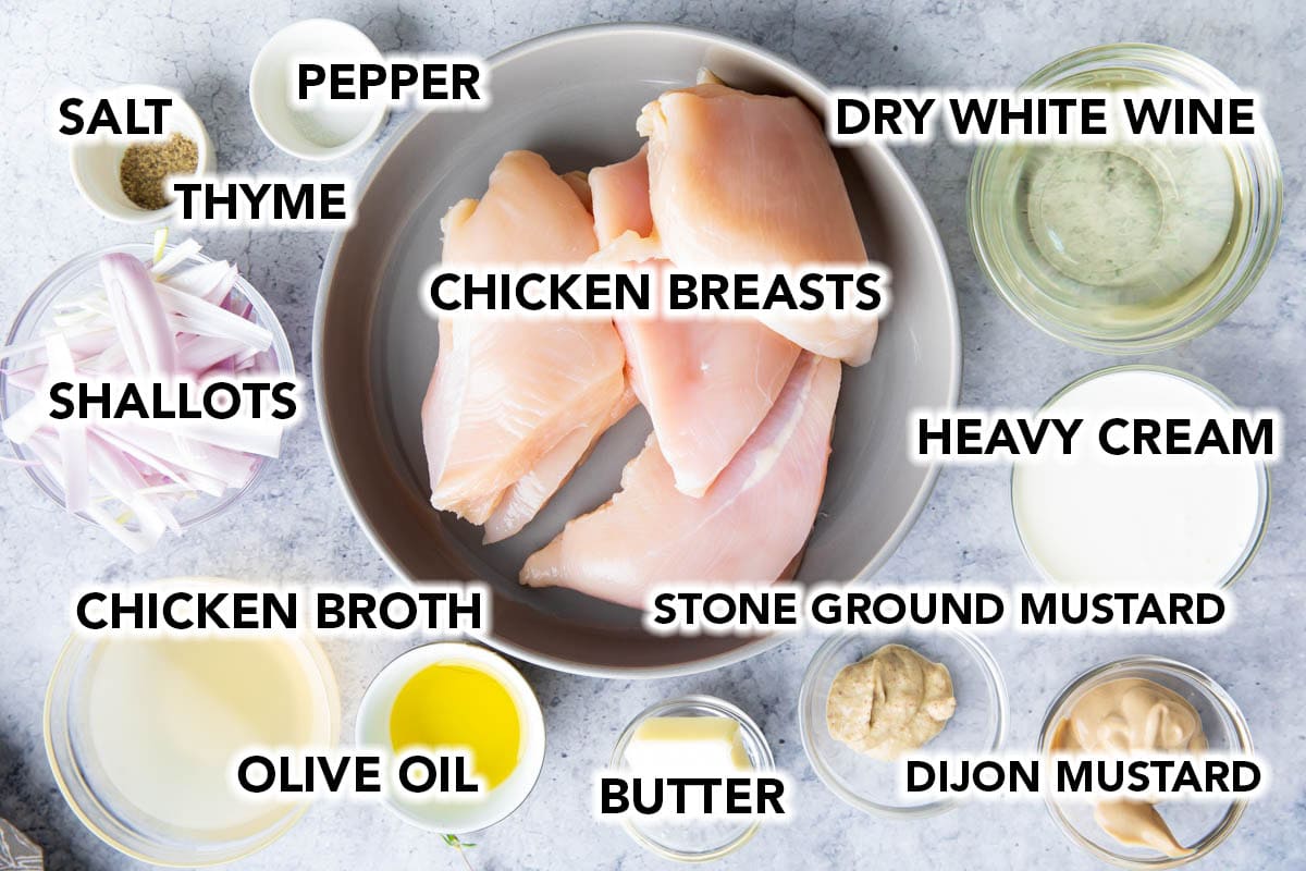 Easy Chicken Dijon recipe ingredients prepped on a table including chicken breasts, salt and pepper, olive oil, butter, shallots, white wine, chicken broth, heavy cream, dijon mustard, stone ground mustard, and thyme.