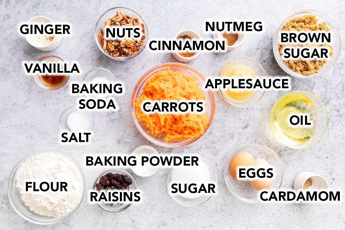 Carrot Cake Cupcakes recipe ingredients in prep bowls, including grated carrots, brown sugar, ground cinnamon, nutmeg, walnuts, flour, baking soda, baking powder, vanilla, raisins, eggs, oil, and more.