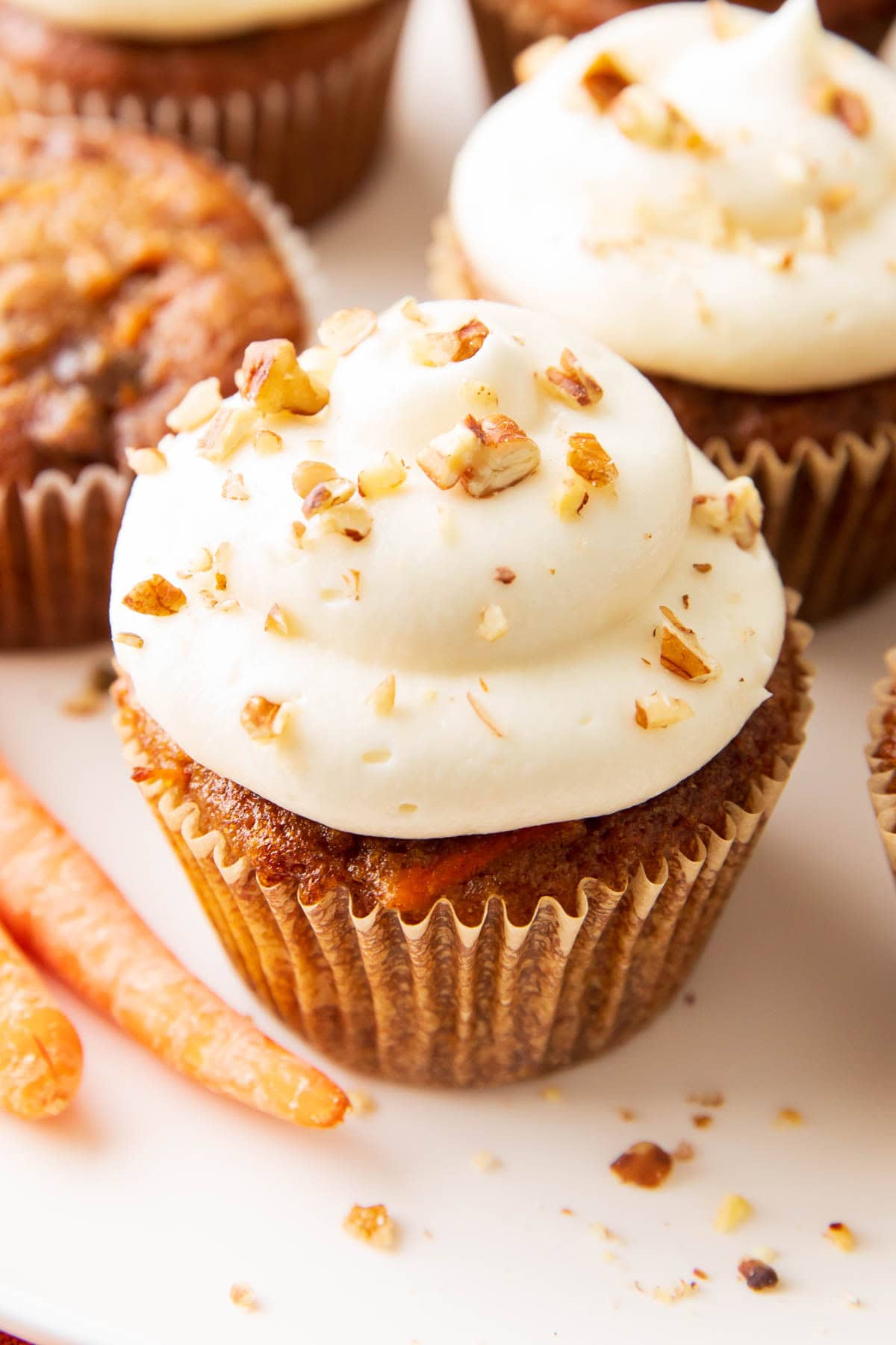 close up of cream cheese icing piped on top of fresh baked cupcakes in parchment liners