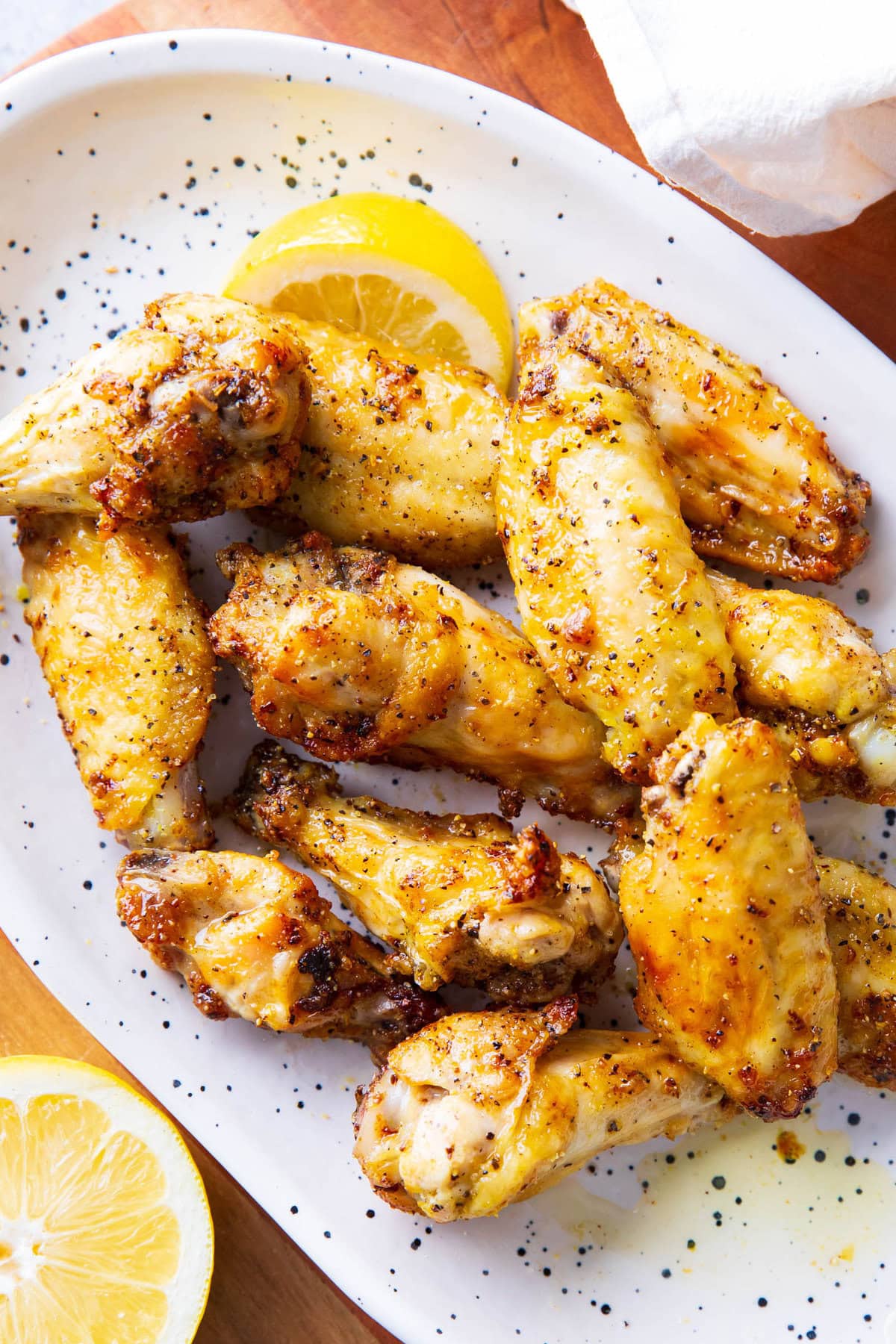 a serving platter of air fryer lemon pepper wings topped with fresh cracked pepper and lemon wedges.