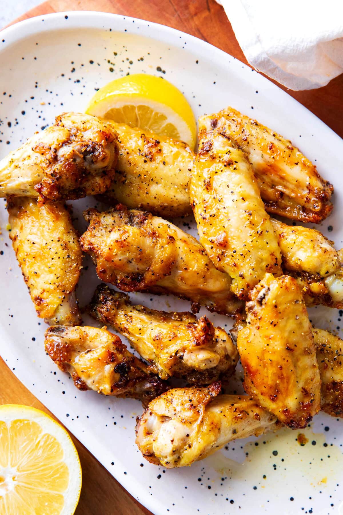 a serving platter of lemon pepper wings topped with fresh cracked pepper and lemon wedges.