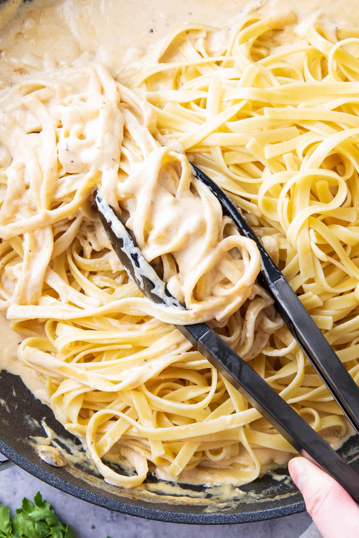 Using tongs to grab and toss al dente pasta in the pan to coat with creamy sauce.