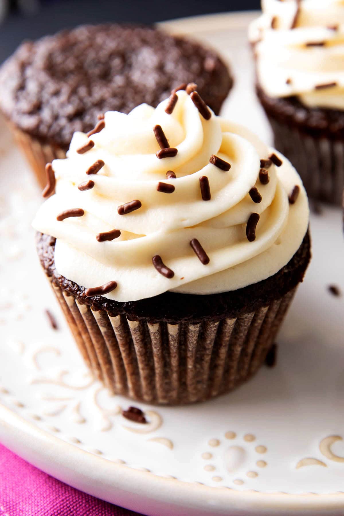 Chocolate sprinkles sit atop chocolate cupcakes with cream cheese frosting.