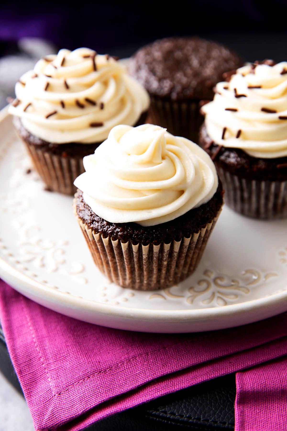 A platter of chocolate cupcakes with cream cheese frosting including some frosted and other plain.