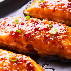 close up of this honey teriyaki salmon to show it perfectly cooked with tasty bits of sesame, ginger, and chili on top.