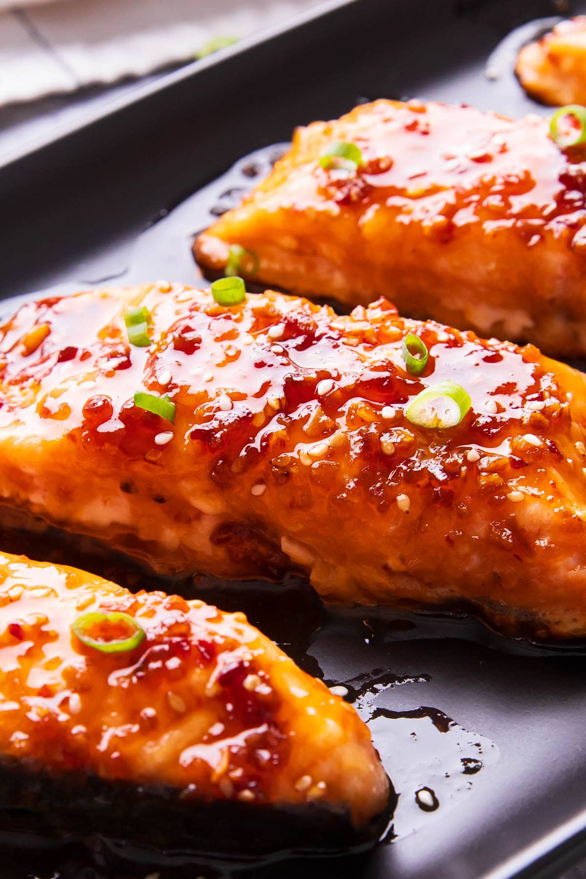 Close up of this honey teriyaki salmon to show it perfectly cooked with tasty bits of sesame, ginger, and chili on top.