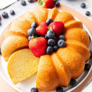 Buttermilk pound cake on a serving platter with berries and one slice sitting on the platter.