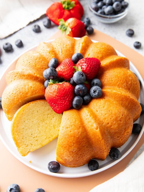 Buttermilk pound cake on a serving platter with berries and one slice sitting on the platter.