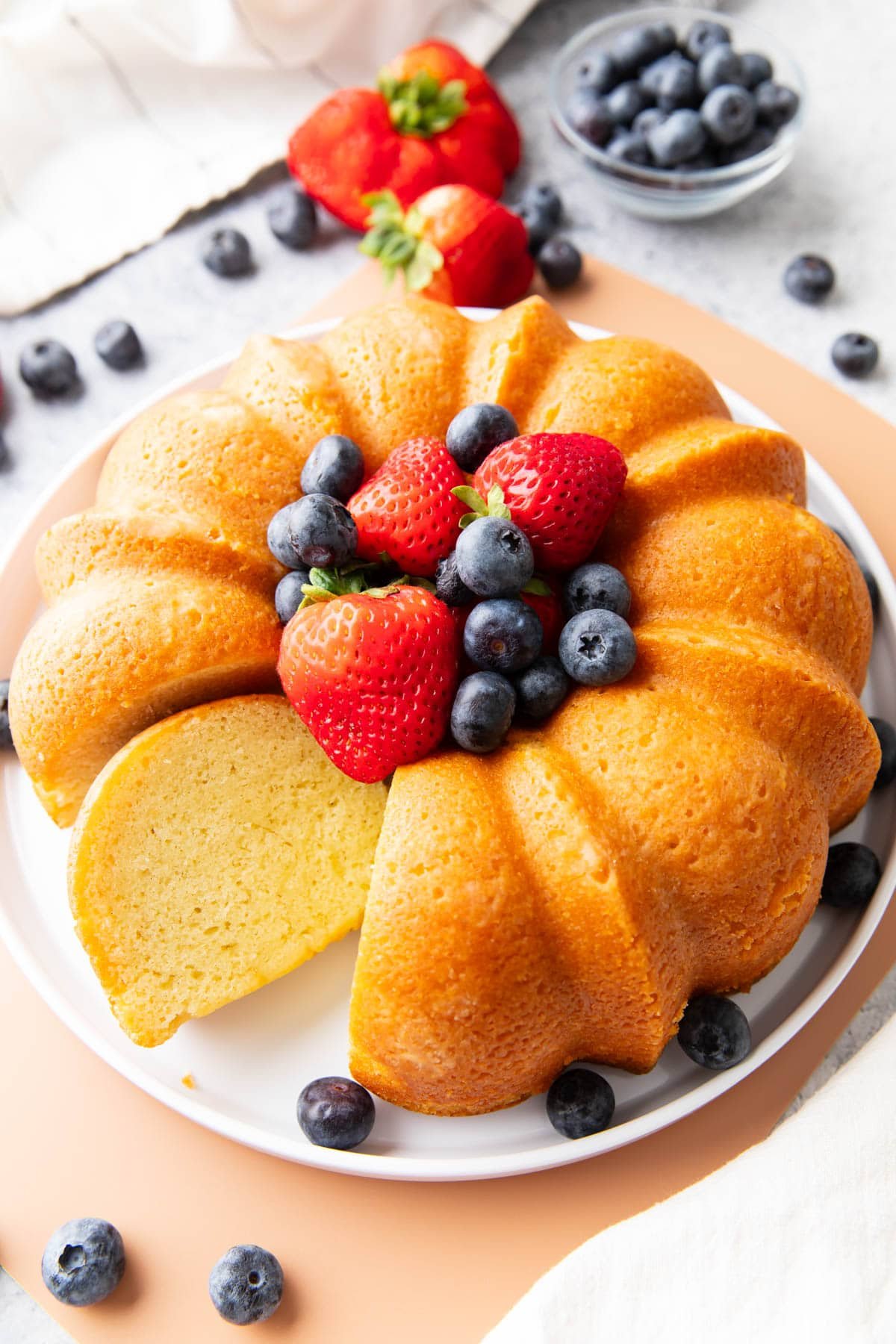 Buttermilk pound cake on a serving platter with berries and one slice sitting on the platter.
