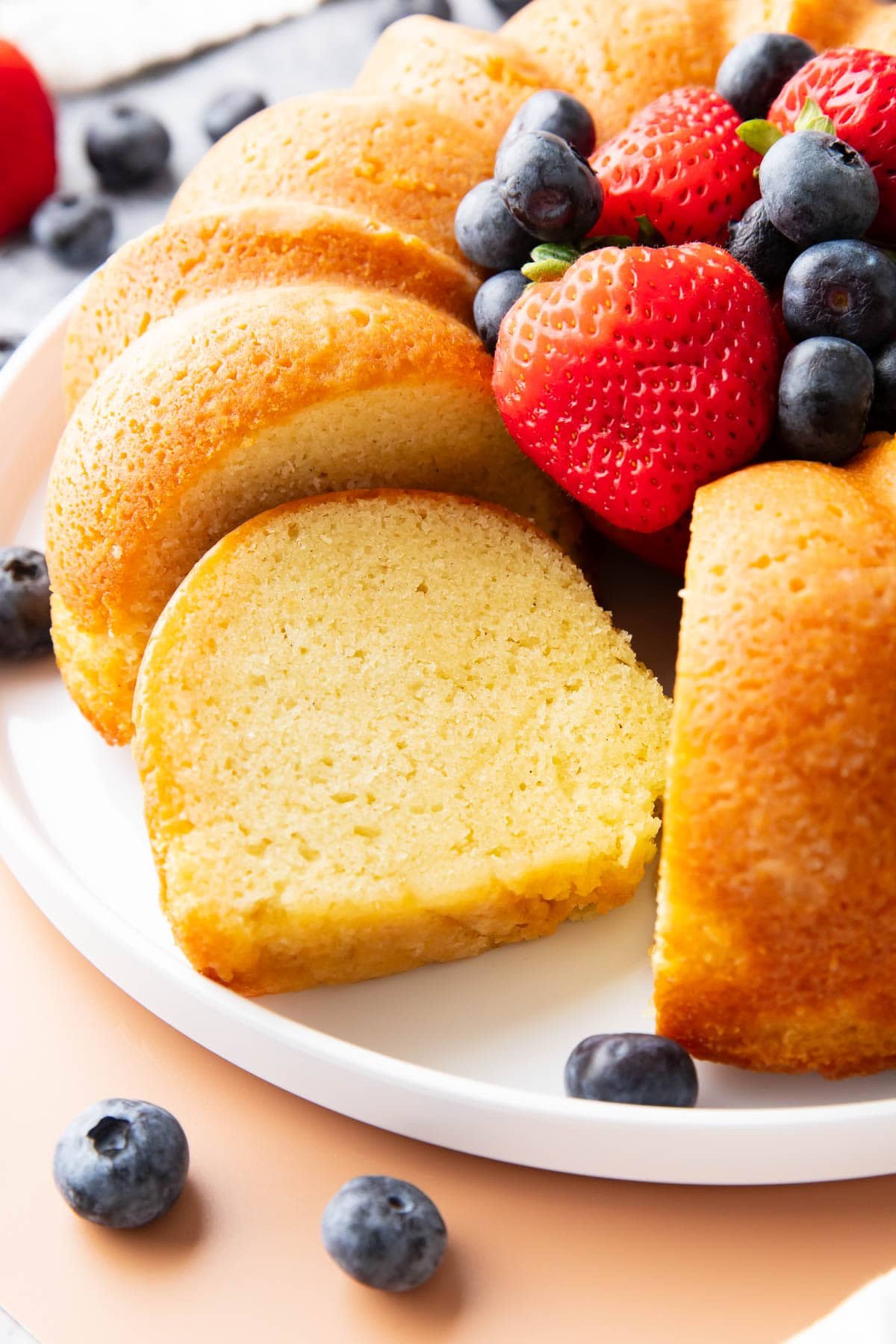 One slice of this buttermilk pound cake recipe sitting on a platter with the whole cake to show the buttery, light yet dense tender crumb.