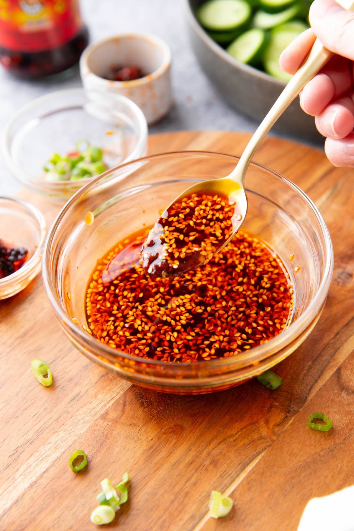Someone spooning this dumpling sauce from a serving bowl with chili oil and scallions in the background.