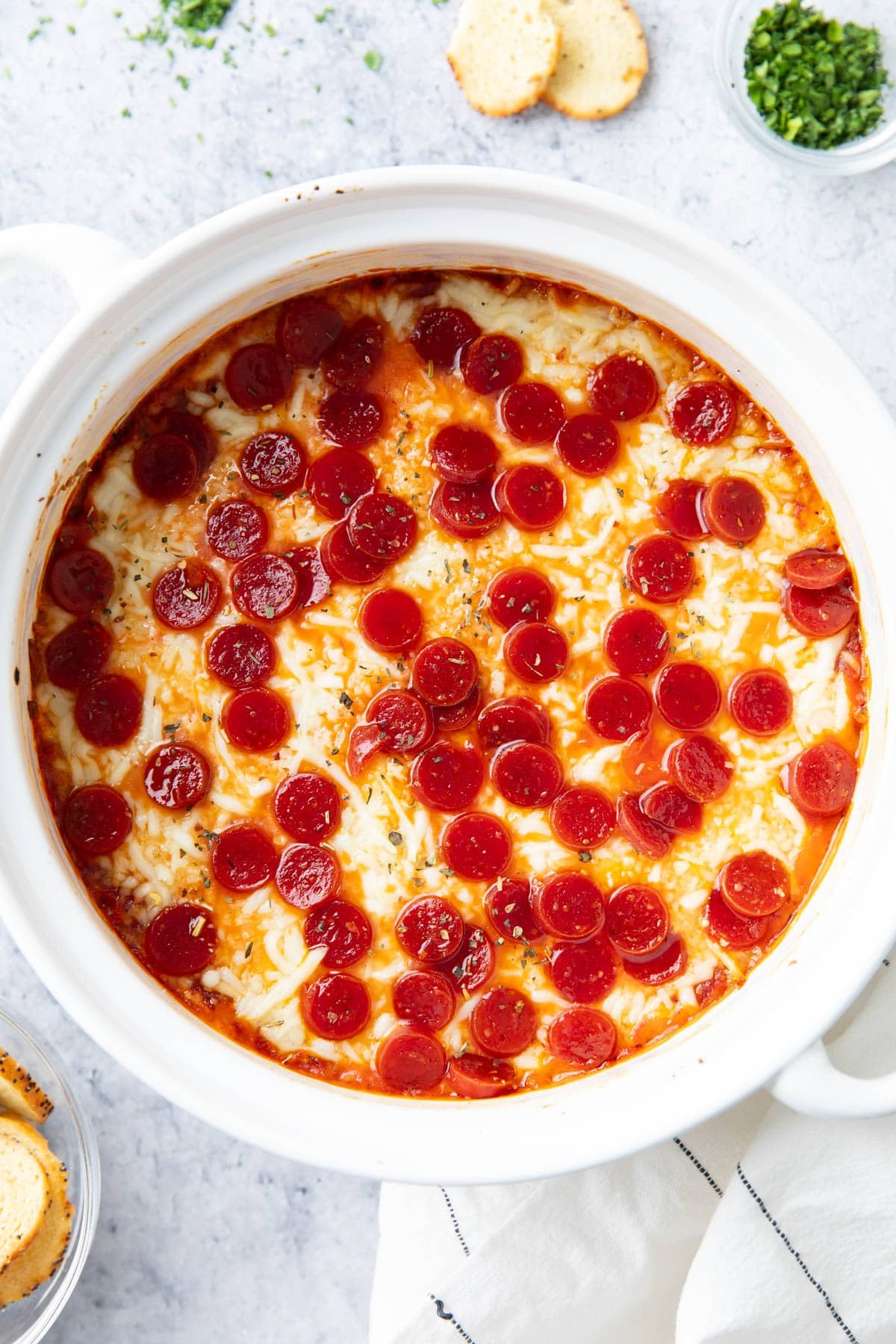 this pizza dip with cream cheese served in a dish topped with pepperoni, served with chips and parsley garnish.