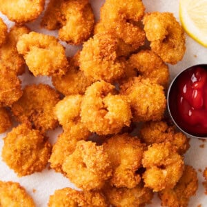 Lots of crunchy fried popcorn shrimp on a paper towel lined pan with lemon wedges and dipping sauce.